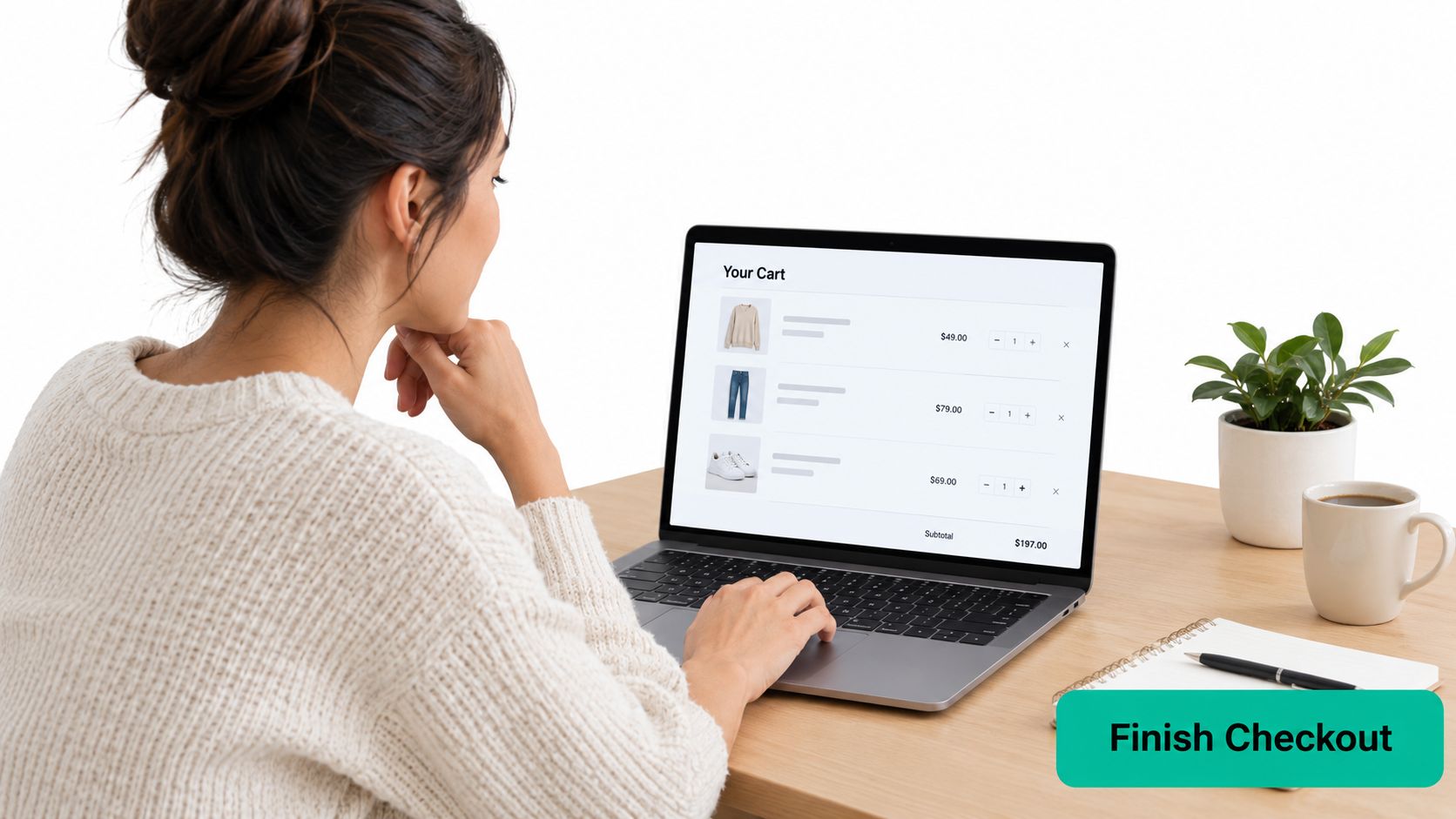 A young woman sitting at a wooden desk viewing an online shopping cart on her laptop.